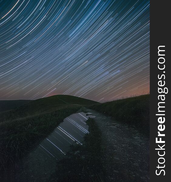 Star trails mirrored in a puddle on a mountain road. Star trails mirrored in a puddle on a mountain road