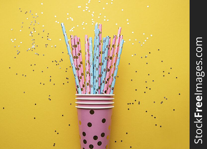 Drinking straws for party and silver stars confetti on yellow background with copy space. Top view of colorful paper disposable eco-friendly straws for summer cocktails