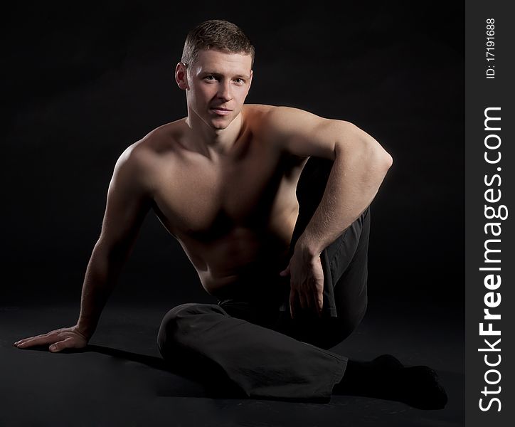 The guy sits in a modeling pose on a black background. The guy sits in a modeling pose on a black background