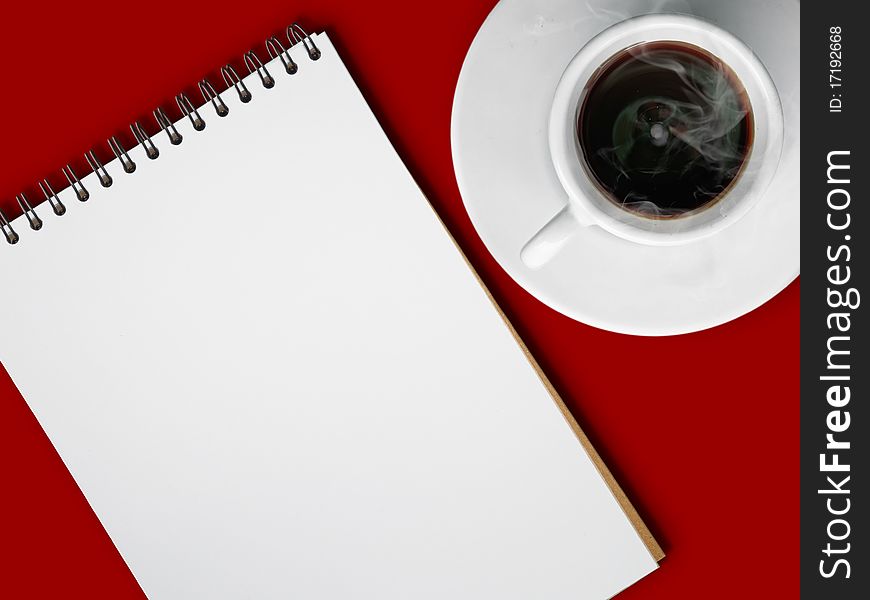 White cup of hot coffee and notebook on red table background
