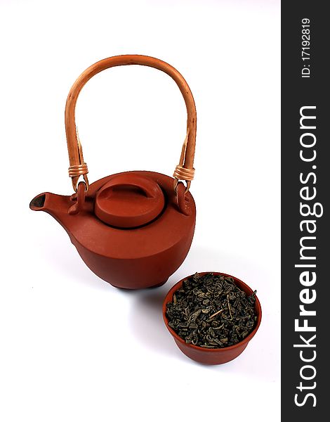 Clay brown teapot and cup with dry green tea on a white background