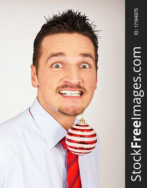 Young man in shirt and red tie has Christmas Ornament between teeth. Young man in shirt and red tie has Christmas Ornament between teeth.