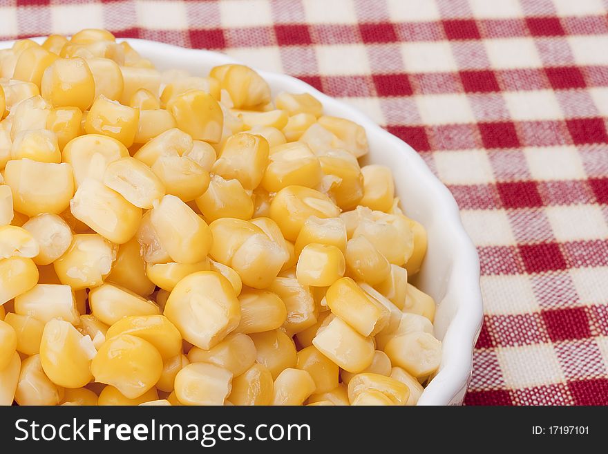 Canned corn in a white bowl on a checkered tablecloth