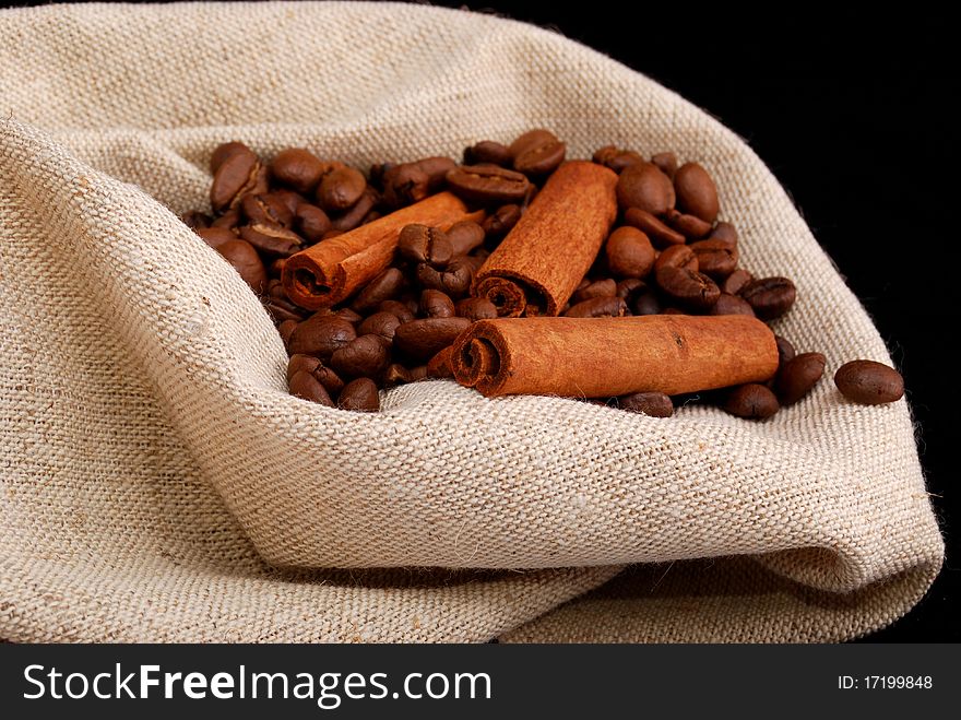 Brown fried grains of coffee and stick cinnamon scattered on a black background