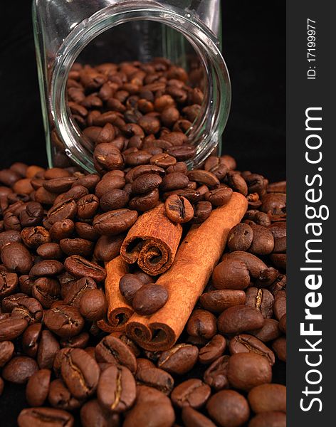 Brown fried grains of coffee and stick cinnamon scattered on a black background