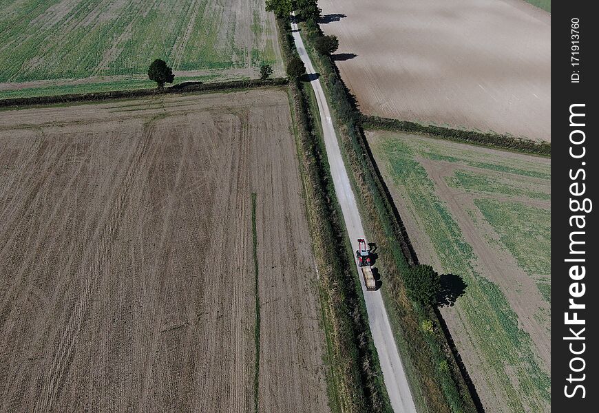 Drone view of a tractor and trailer on a long rural road between flat ploughed fields. Drone view of a tractor and trailer on a long rural road between flat ploughed fields