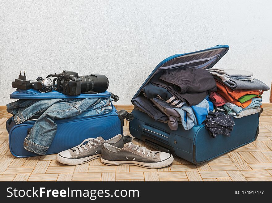 Open blue suitcase with a lot of clothing, impossible to close, preparing for vacations, white background. Open blue suitcase with a lot of clothing, impossible to close, preparing for vacations, white background