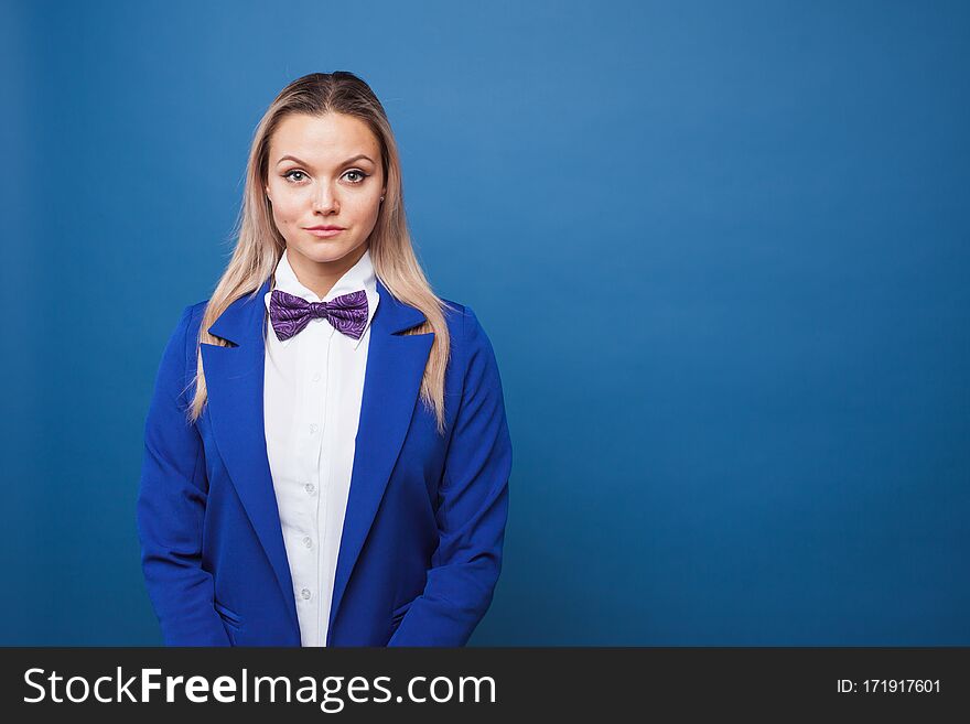 Cute girl in blue jacket with bow tie on blue background. Funny business portrait, copy space