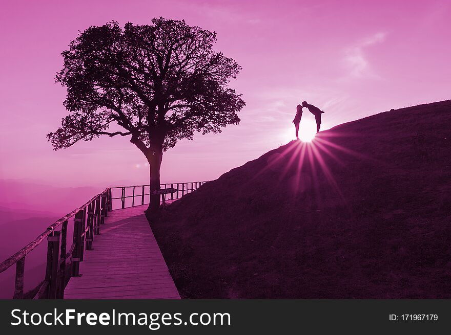 Couple silhouette on hill and lonely tree, The sun is falling down behind with lights flare On the top of Doi Pui Co,  Popular tourist attraction in Mae Hong Son, Thailand. Couple silhouette on hill and lonely tree, The sun is falling down behind with lights flare On the top of Doi Pui Co,  Popular tourist attraction in Mae Hong Son, Thailand