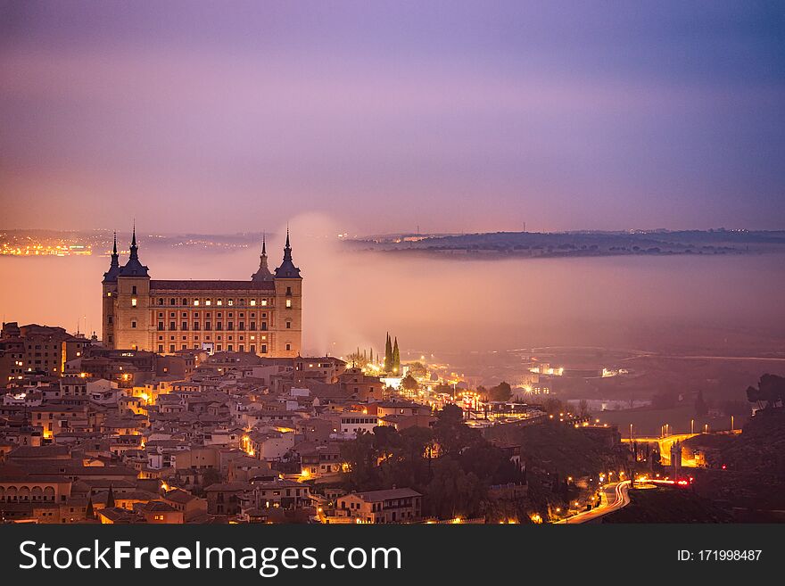 Sunrise in the historic and amazing Downtown Toledo. Alcazar is surrounded by fog. Foggy morning with city lights in Toledo, Spain.