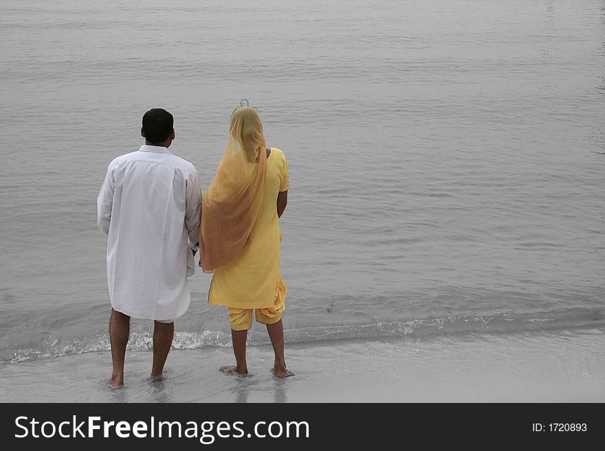 A pair of indians standing at the water's edge at a beach. They were staring out to sea. The water is monochrome to make them stand out. A pair of indians standing at the water's edge at a beach. They were staring out to sea. The water is monochrome to make them stand out.