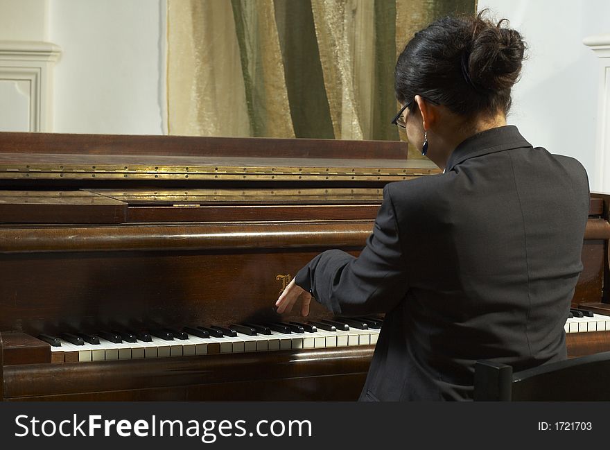 Portrait of a female piano teacher looking downward as she plays piano. Shot from back view. Portrait of a female piano teacher looking downward as she plays piano. Shot from back view.