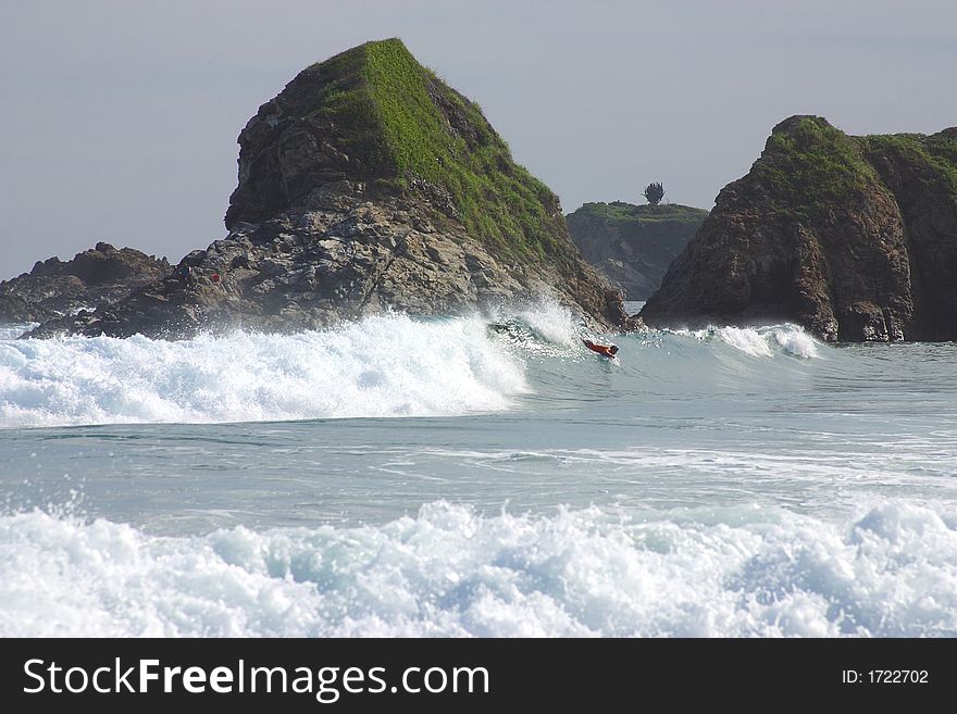 Partial view of a wave with a surfer and a small cliff in the bay of San Agustinillo in the southern state of Oaxaca in  Mexico, Latin America