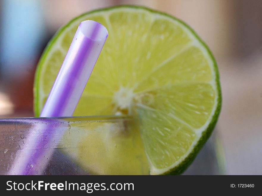 Purple and white stripped straw and partial view of a slide of a lemon on a glass of lemonade