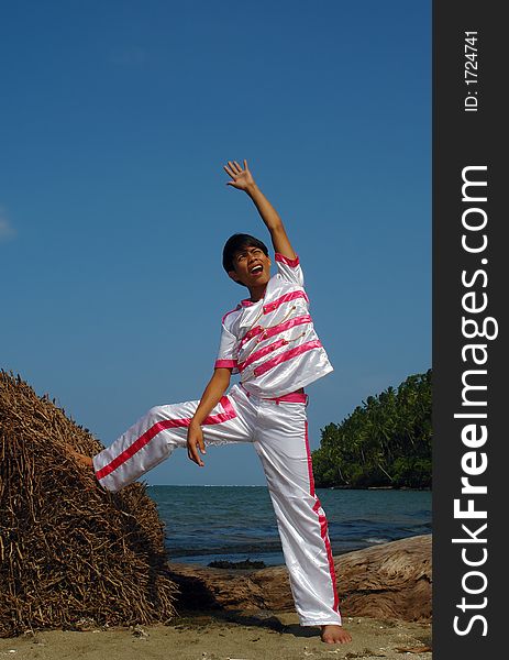 Asian boy in modern dance costume on tropical pristine beach posing and pointing in the sky. Asian boy in modern dance costume on tropical pristine beach posing and pointing in the sky.