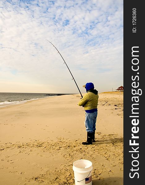 A lone fisherman checks his fishing line on the deserted beach as he surf fishes on a cold, winter morning. A lone fisherman checks his fishing line on the deserted beach as he surf fishes on a cold, winter morning.