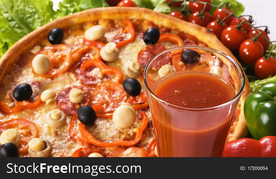 Closeup picture of a pizza with vegetables and glass of tomato juice