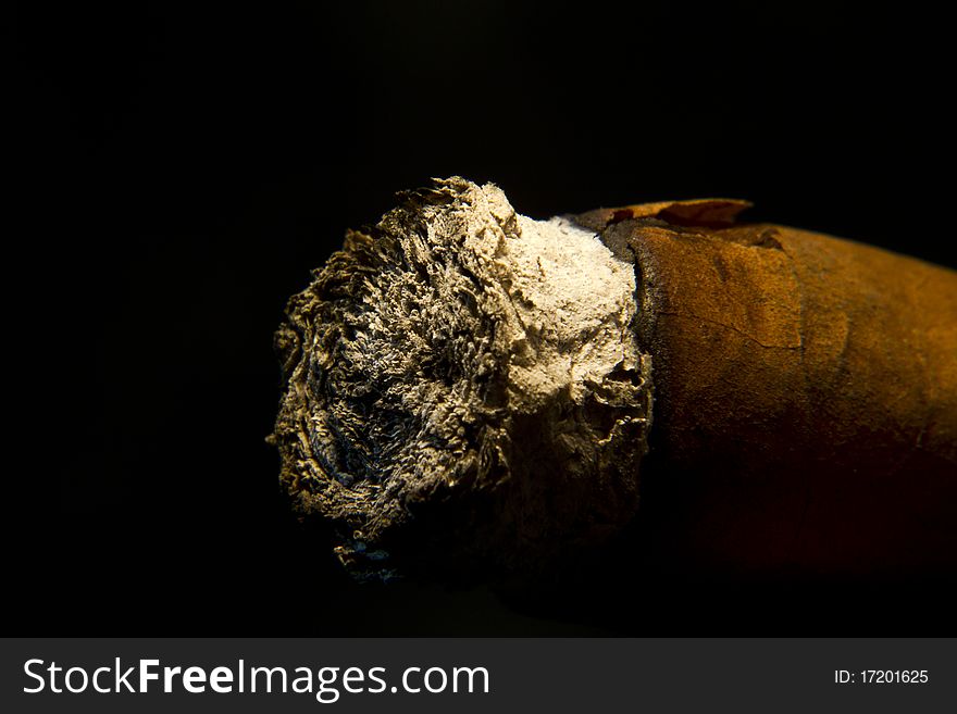 Used cigar with its ash at the front, lit from above on black background. Used cigar with its ash at the front, lit from above on black background.