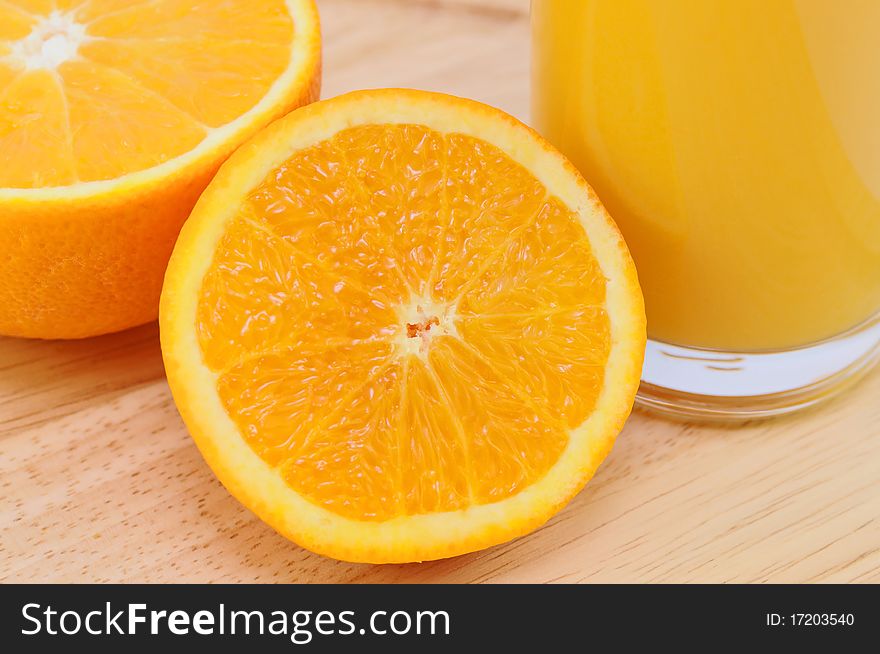 Glass of fresh orange juice with orange halves on wooden surface