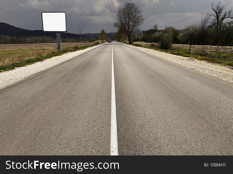 Empty road through fields with blank billboard beside