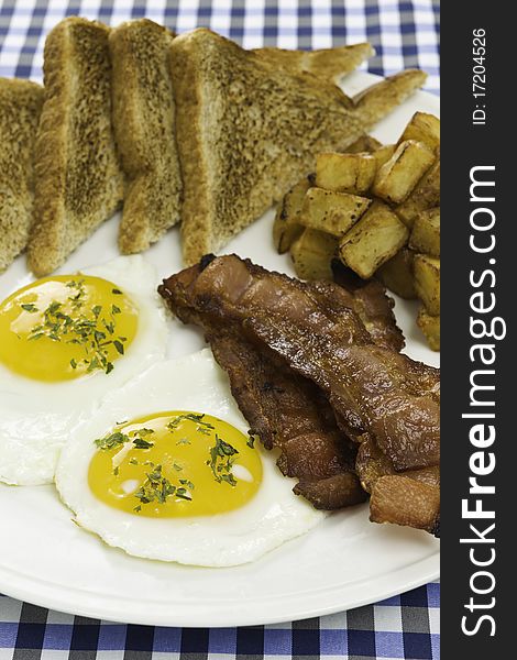 Breakfast meal on a white plate with two eggs,potato,toasted bread and bacon. Orientation : vertical Concept : mealtime,food,morning. Breakfast meal on a white plate with two eggs,potato,toasted bread and bacon. Orientation : vertical Concept : mealtime,food,morning