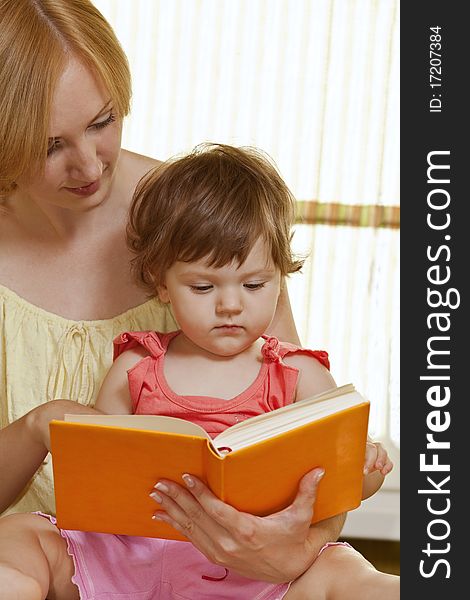 Young mother with her daughter reading book at home