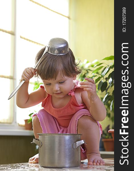 Little girl with a pan and ladle on her head sitting on a table