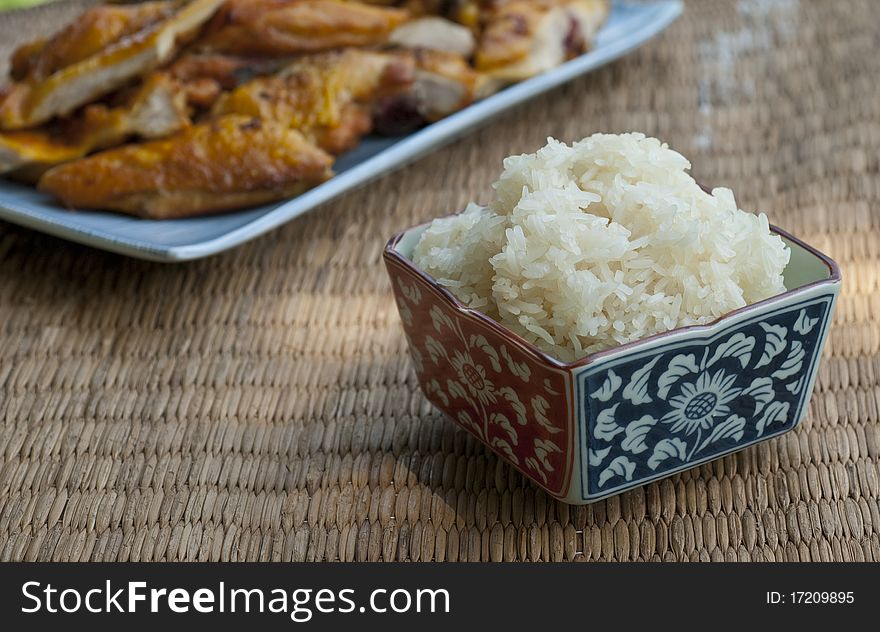 A bowl of sticky rice with grilled chicken in the background