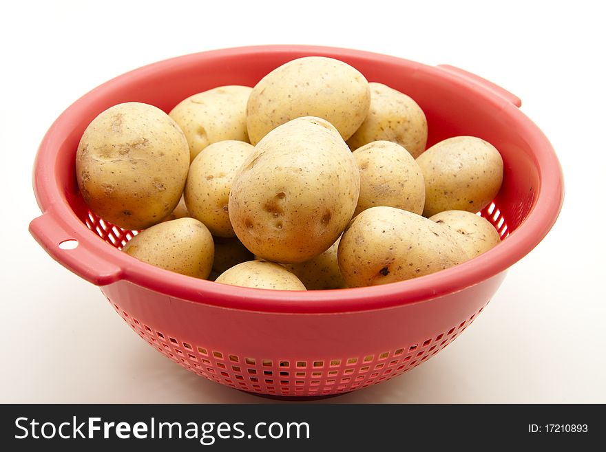 Raw potatoes in the red kitchen sieve. Raw potatoes in the red kitchen sieve