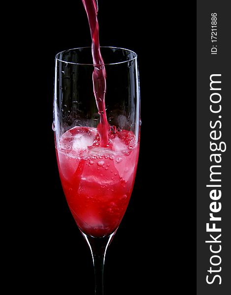 Pouring red drink into the glass isolated on black background