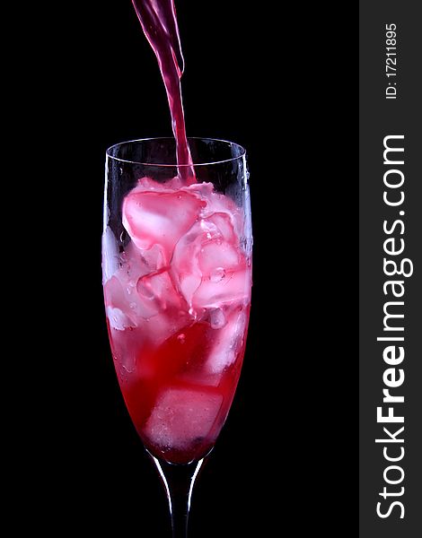 Red cocktail being poured into a glass isolated on black background