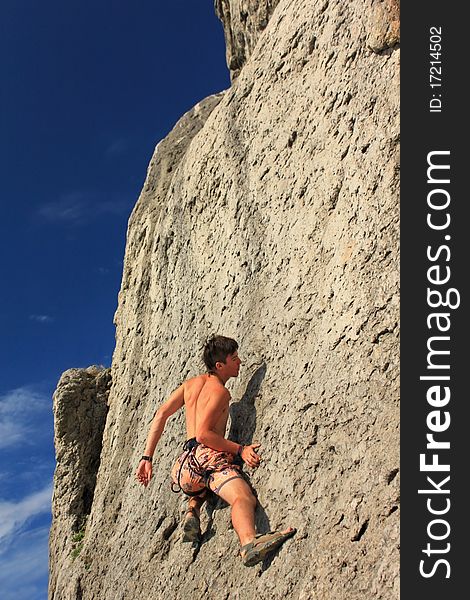 A guy climbs on a rock against the blue sky. A guy climbs on a rock against the blue sky
