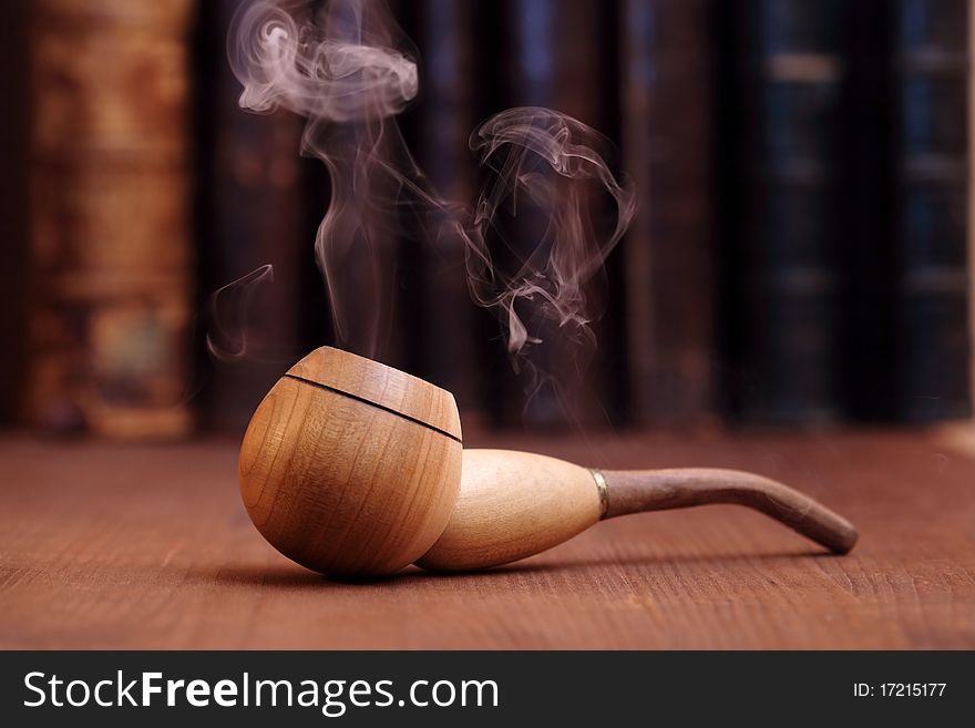 Smoking tobacco pipe on wooden background with old books