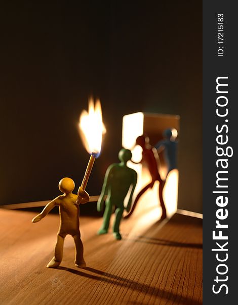 Few plasticine men with lighting match entering to dark room. Conceptual composition with open door made from paper