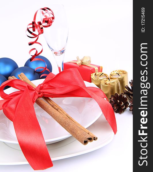 Christmas or New Year's table - a plate decorated with cinnamon sticks and ribbon, a glass, christmas balls, candles, gift and cones