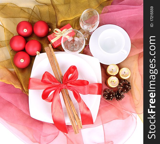 Christmas table-a plate decorated with cinnamon sticks and ribbon, a cup, glasses, christmas balls, candles, gift and cones