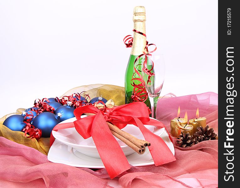 Christmas or New Year's setting - a plate decorated with ribbon and cinnamon sticks, a bottle of champagne, a glass, candles, christmas balls