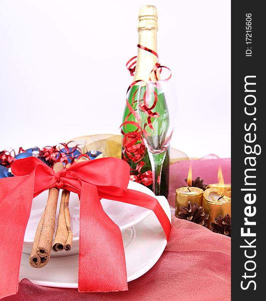 New Year's or Christmas setting - a plate decorated with ribbon and cinnamon sticks, a bottle of champagne, a glass, candles, a gift , cones, christmas ball