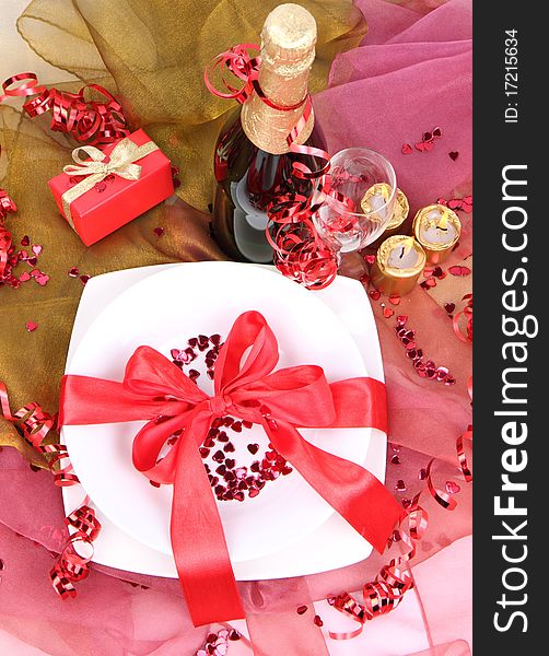 New Year's or Valentine's setting - a plate decorated with ribbon and heart shaped confetti, a bottle of champagne, a glass, candles, a