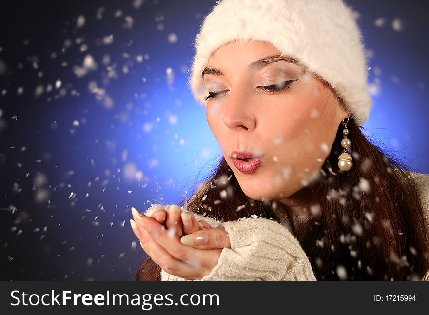 Cute young woman blows snowflakes