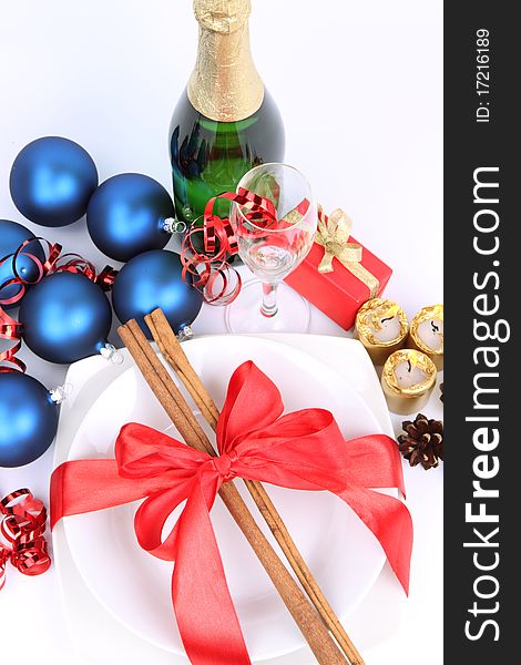 Christmas or New Year's setting - a plate decorated with ribbon and cinnamon sticks, a bottle of champagne, a glass, candles, christmas balls