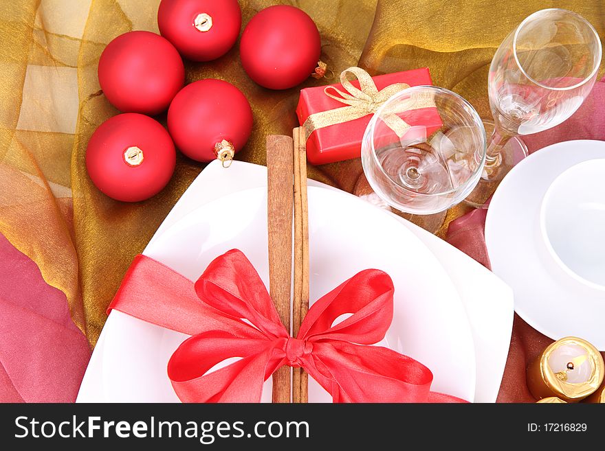 Christmas or New Year's setting - a plate decorated with cinnamon sticks and ribbon, christmas balls, candles and wine glasses in close up