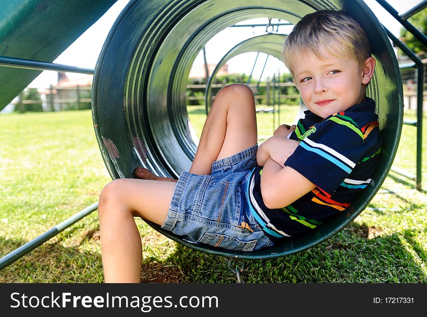 Young white boy sits in tunnel at the playground. Young white boy sits in tunnel at the playground
