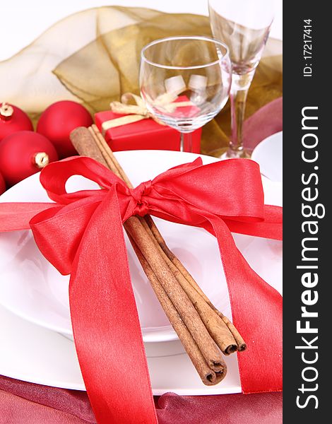 Christmas tableware, decorated with cinnamon sticks, ribbon, christmas balls and a gift in close up. Christmas tableware, decorated with cinnamon sticks, ribbon, christmas balls and a gift in close up