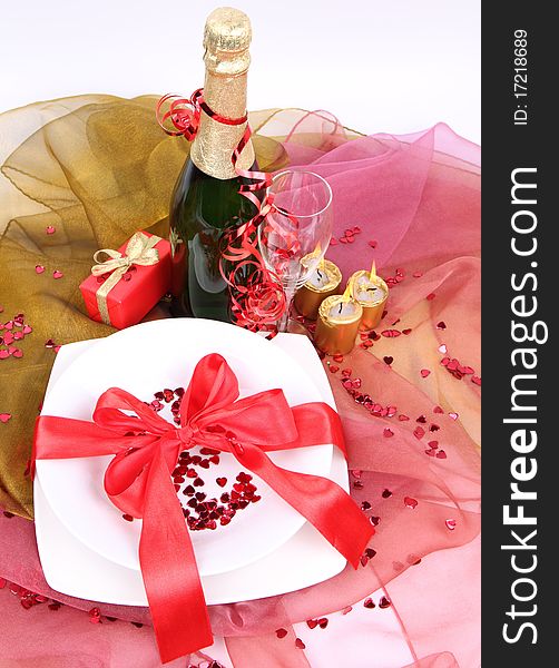 New Year's or Valentine's setting - a plate decorated with ribbon and heart shaped confetti, a bottle of champagne, a glass, candles, a gift in close up