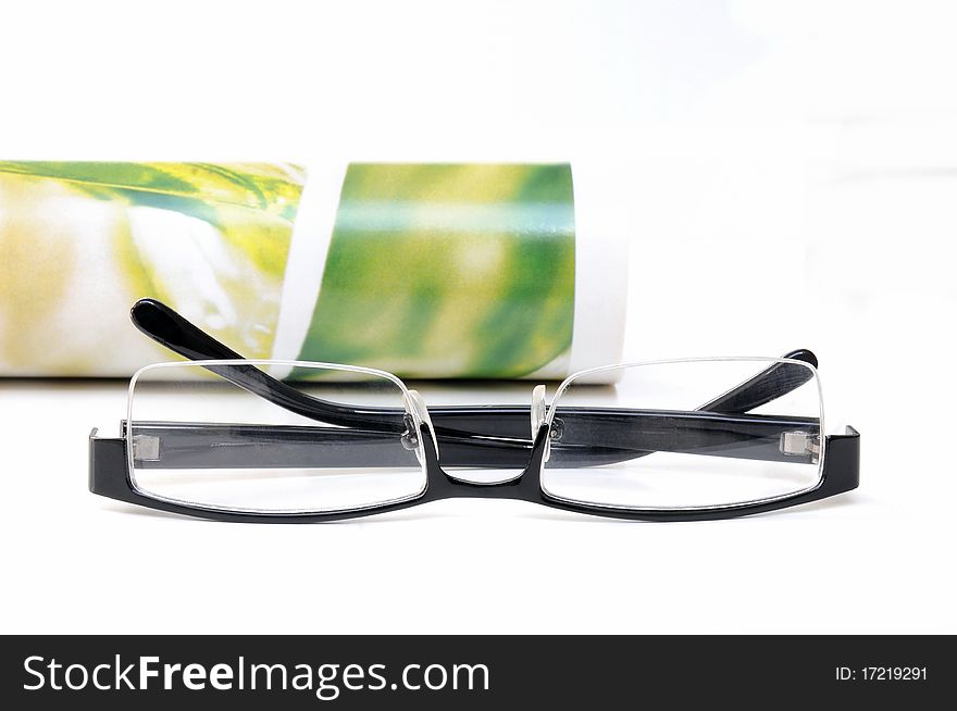 Rolled magazine with glasses over white background