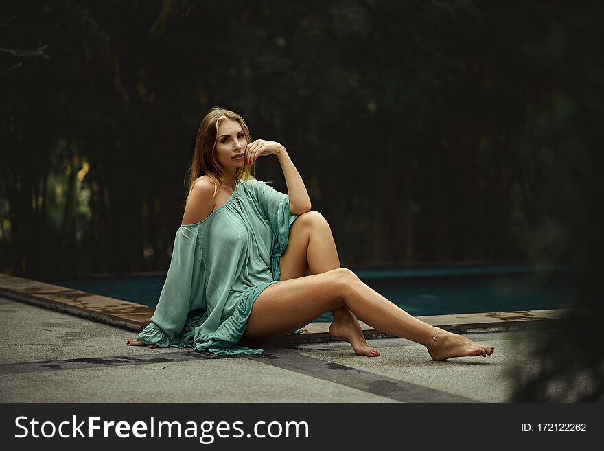 Fashion photo of beautiful young woman wearing green dress, relaxing on luxury villa