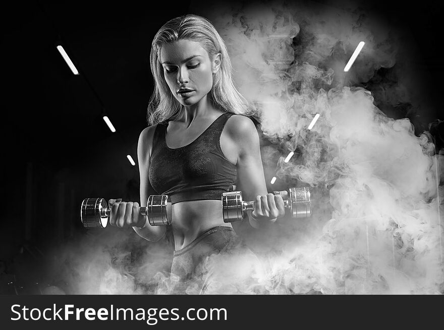 Charming sportswoman posing in the gym with dumbbells. The concept of bodybuilding, fitness, stretching, healthy eating. Mixed media