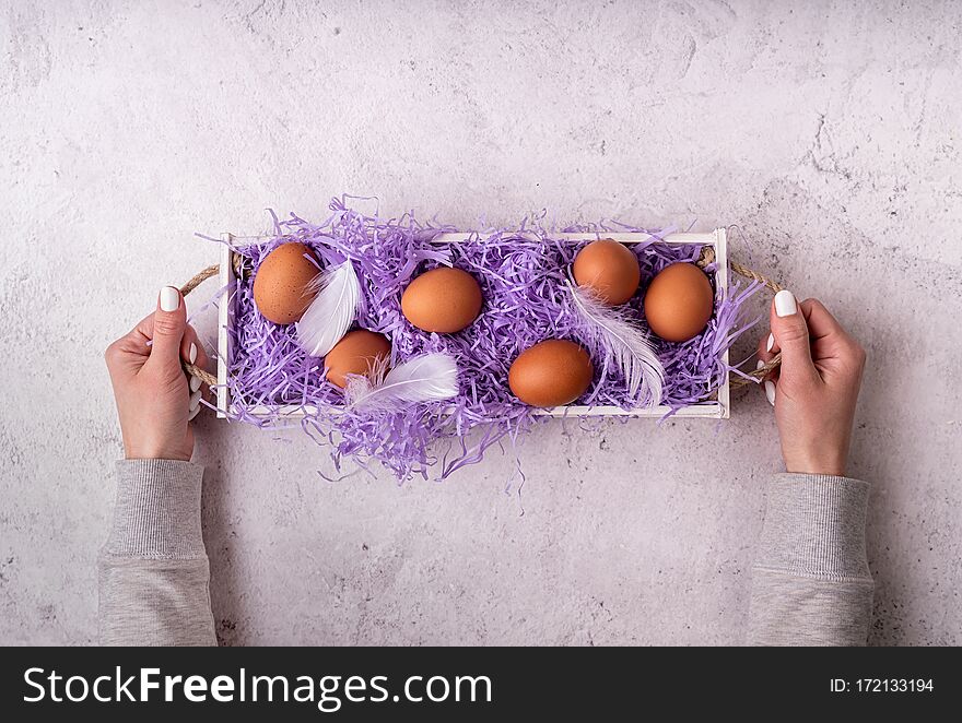 Woman hands holding white wooden box with chicken eggs on white marble background top view flat lay
