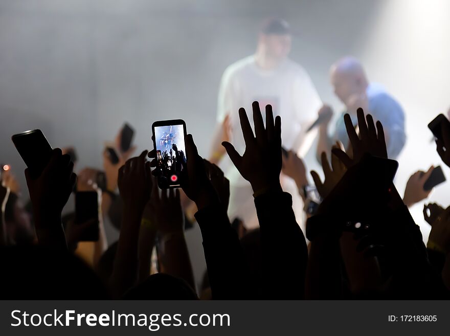 Hand with a smartphone records live music festival, Taking photo of concert stage. Party at nightclub with crowd of people raising